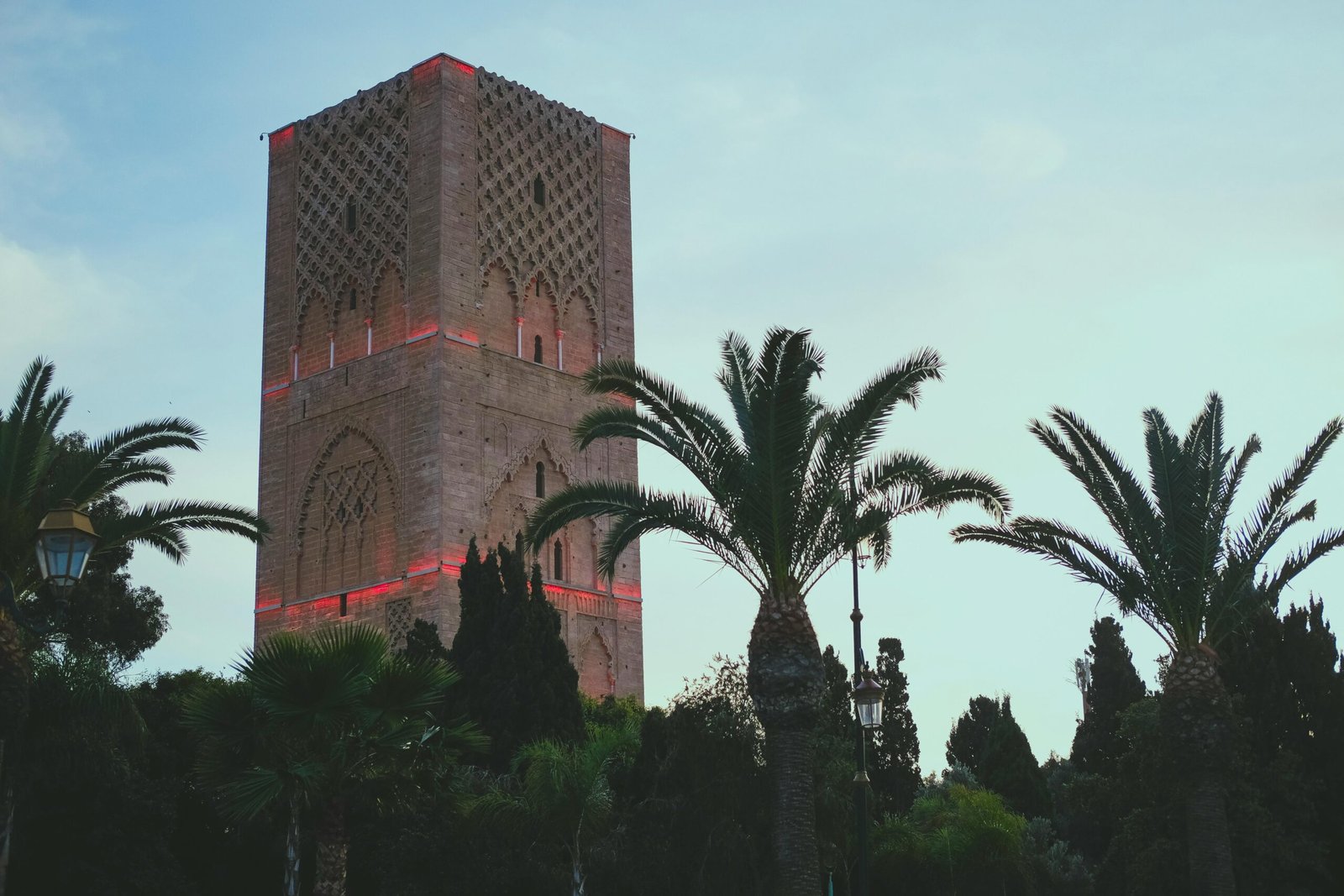 The iconic Hassan Tower surrounded by palm trees at dusk in Rabat, Morocco.